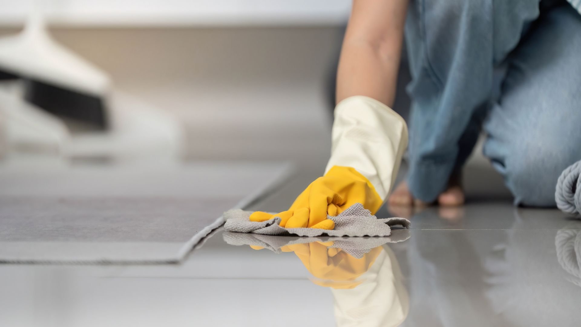 Person wearing yellow gloves cleaning floor with gray cloth