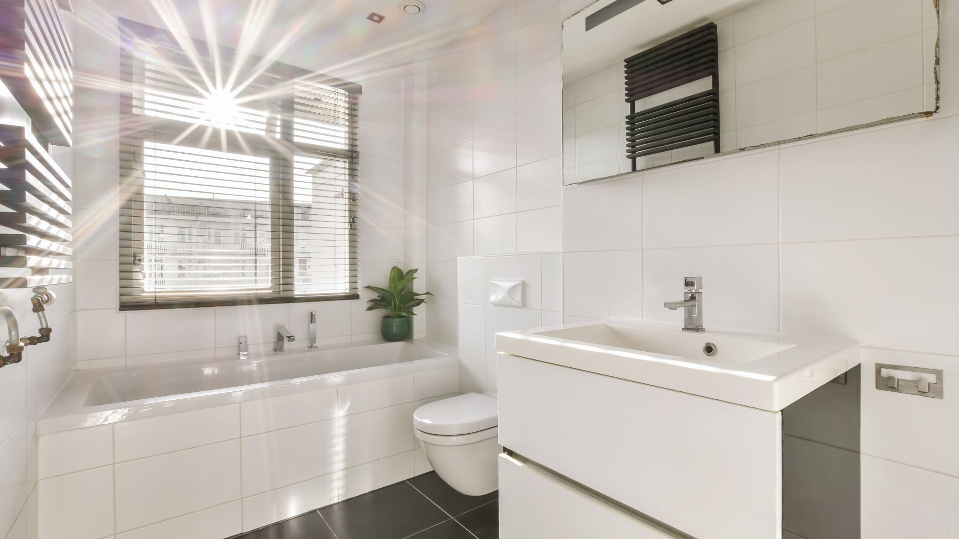Modern white bathroom with bathtub, sink, and sunlight through blinds