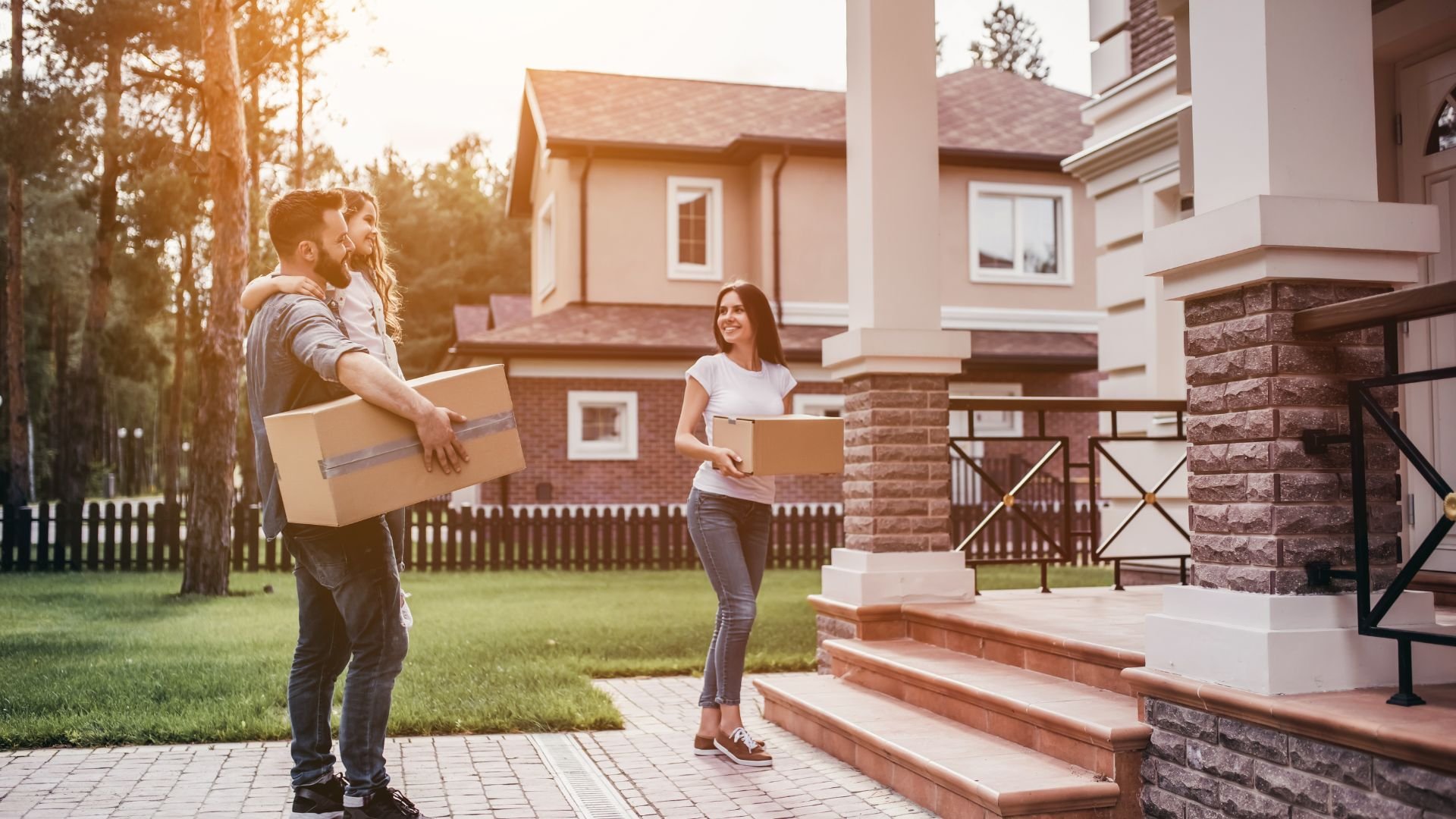Couple carrying moving boxes in front of new suburban home at sunset